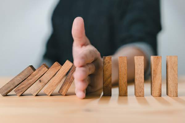 intervention a hand stopping a row of dominoes from falling.