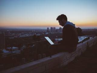 a man sitting on a ledge working on a laptop