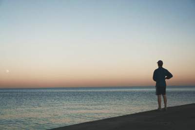 man standing on a beach looking at the water at sunset