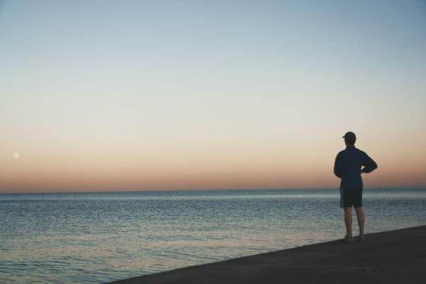 man standing on a beach at sunset looking at the water