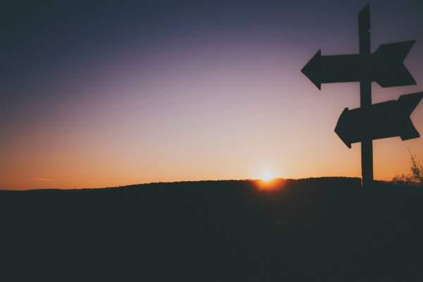 purple sunset with shadwowed streetsign of arrows in the foreground.